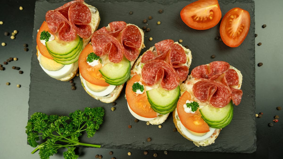 Delicious open-faced sandwiches with salami, cucumber, and tomato on a slate board.